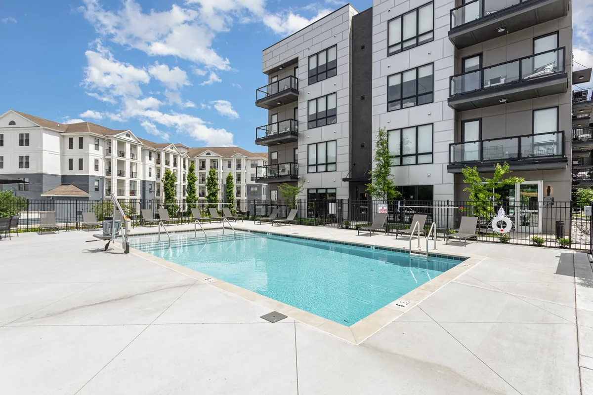 An inviting exterior view of a swimming pool surrounded by balconies and lush greenery. The scene captures guests or residents swimming, sunbathing, and socializing, suggesting both privacy and community within the resort-like environment.