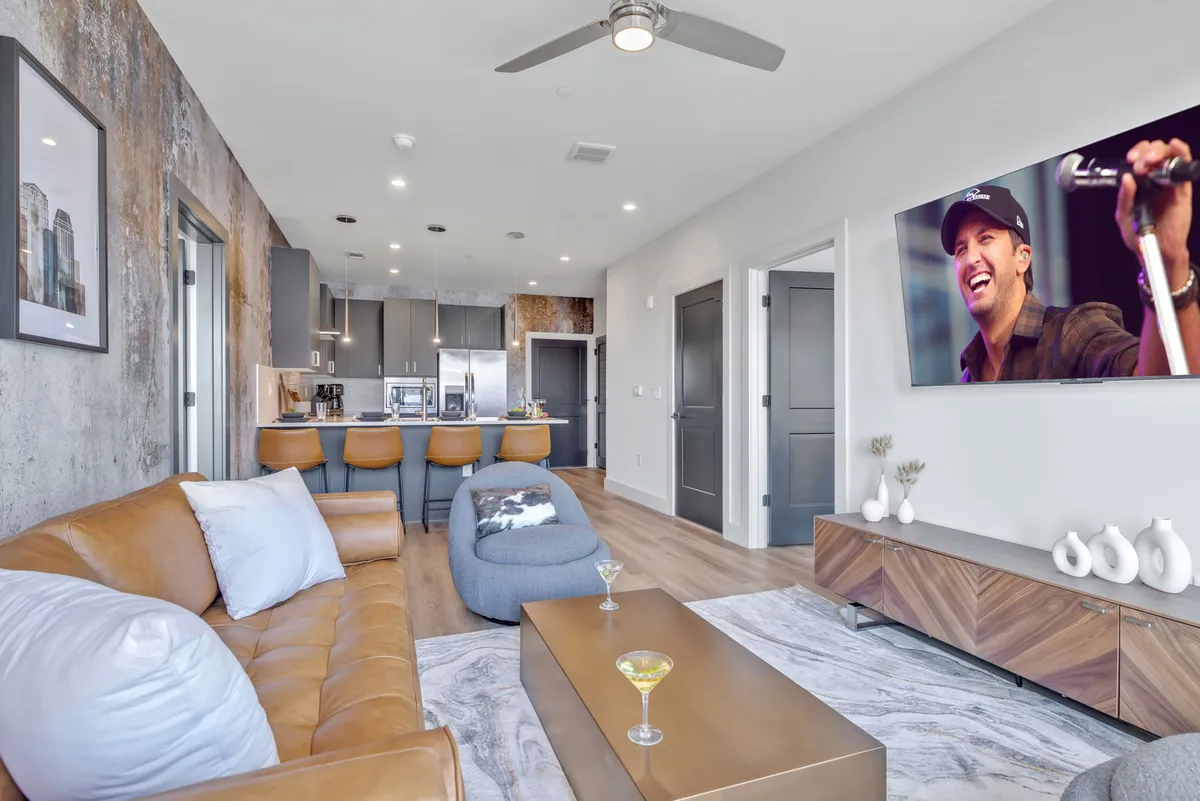 A contemporary open-plan living space with a leather sofa, kitchen island, and a TV displaying a performer. The room exudes a relaxed, welcoming vibe ideal for entertaining or unwinding.